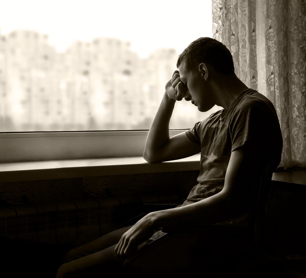 a black and while photo of a depressed white man at a window, looking to our left