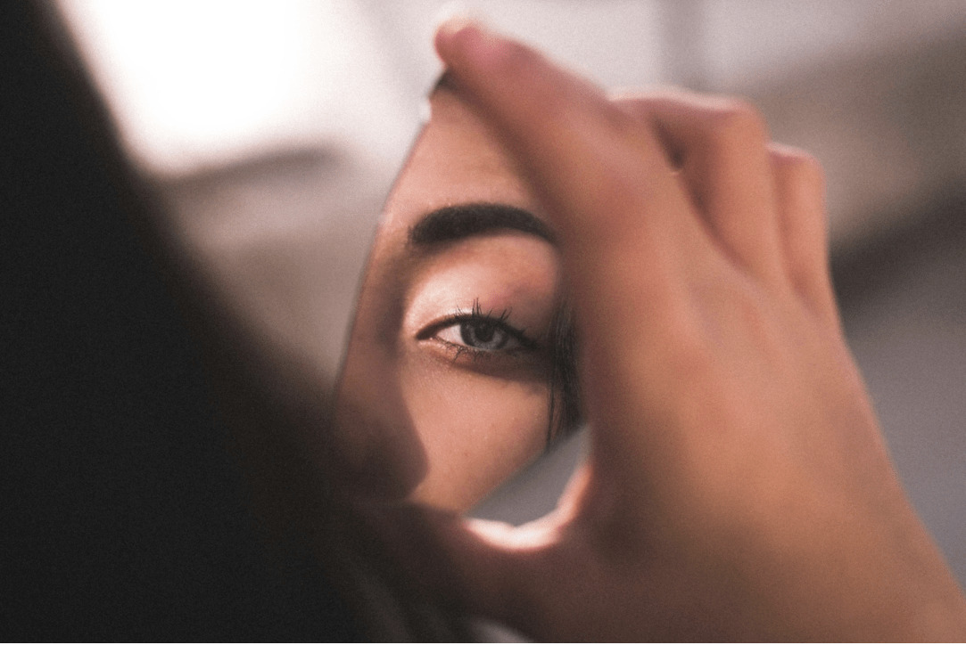 the girl looking at her eye in a mirror | National Social Anxiety Center