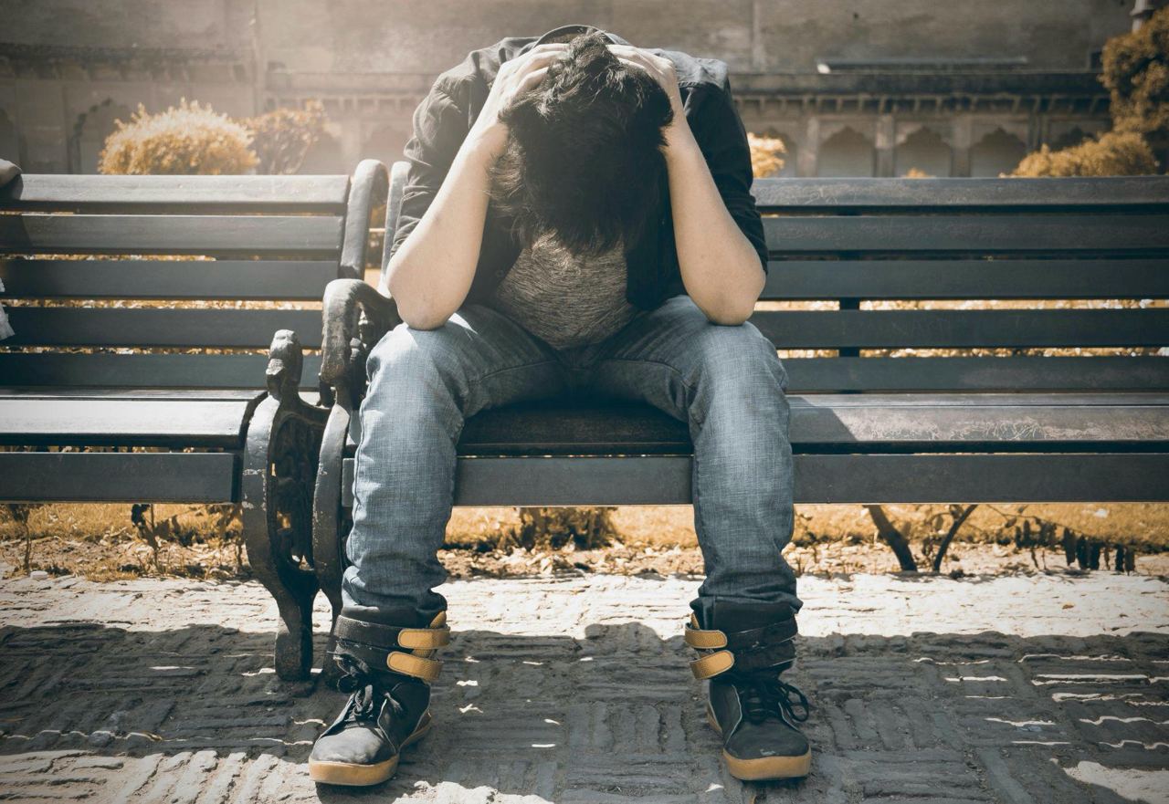 he young man sitting on a bench with his head down